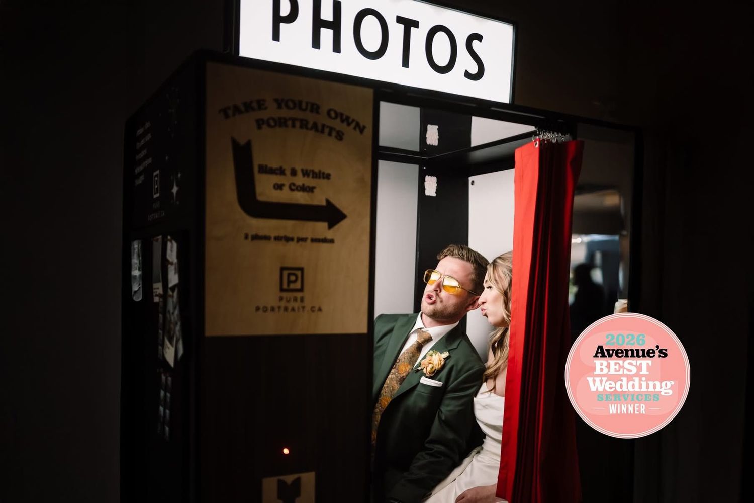 Woman posing inside a vintage photo booth with red curtain backdrop and illuminated PHOTOS sign.