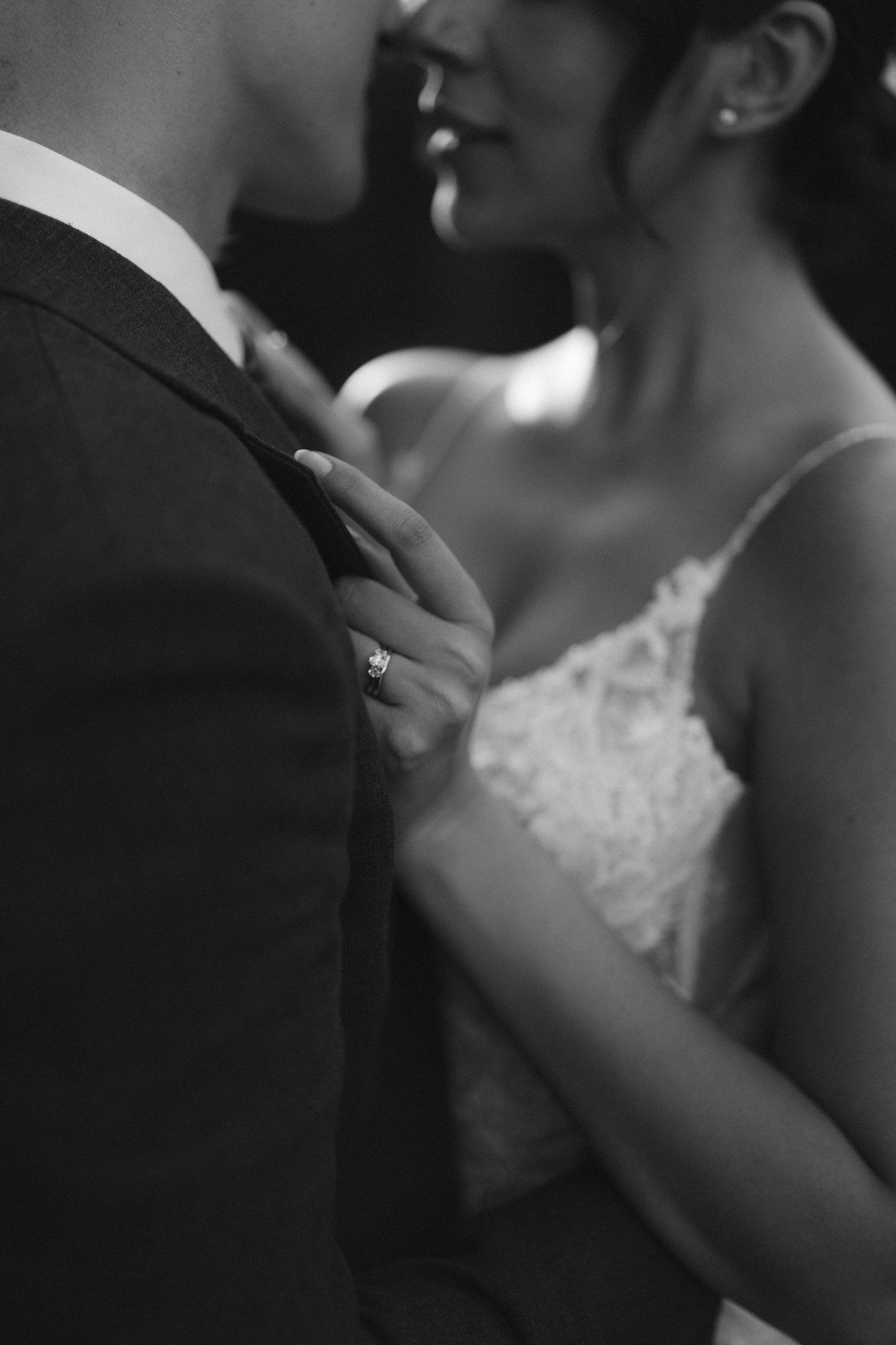 Bride in elegant backless wedding gown with bow, standing by window in black and white photo.
