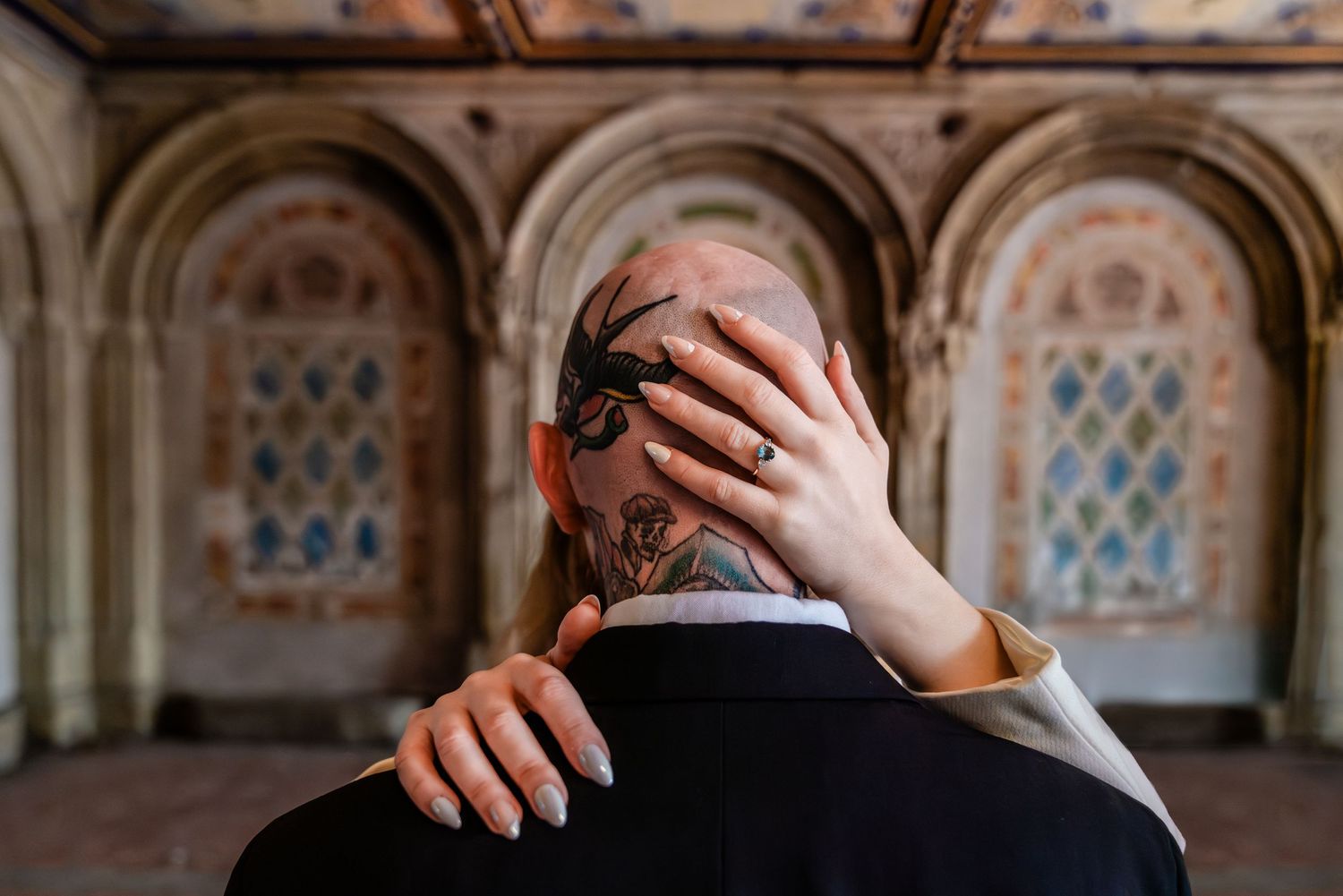 Couple embracing at Bethesda Terrace, man with spider head tattoo, woman with engagement ring on shoulder.