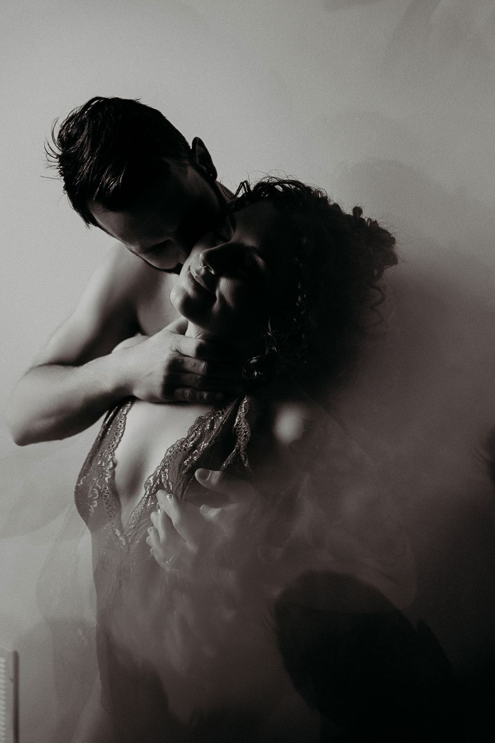 Black and white romantic couple embracing in misty atmosphere, man kissing woman's neck in intimate pose.