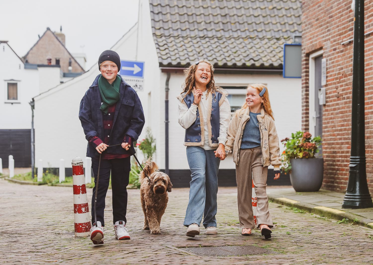 Family walking dog together on cobblestone street in casual winter attire.