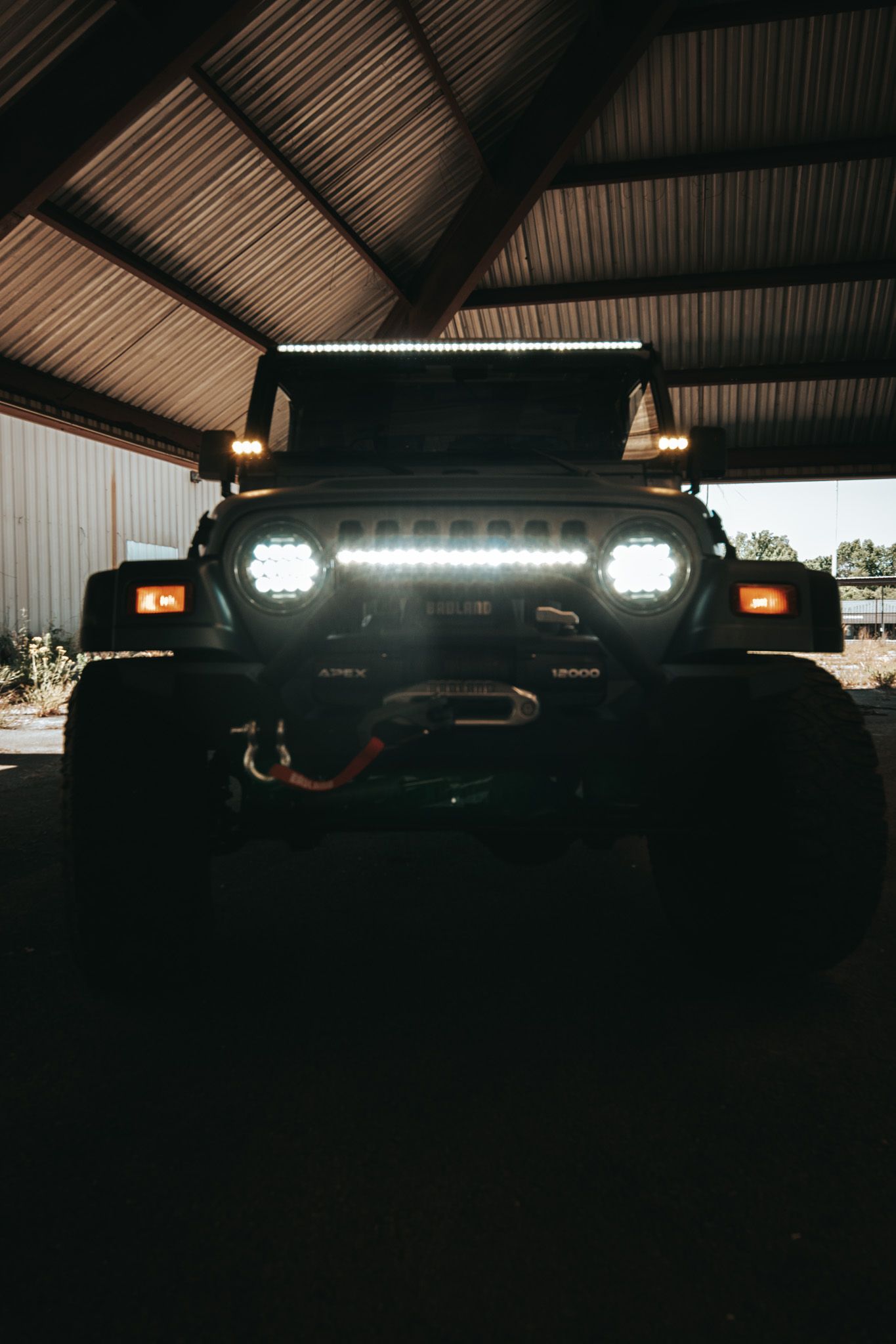 Front view of a Jeep with bright LED light bar and headlights illuminated in dark garage.