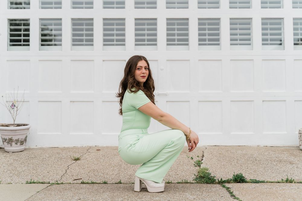 A person in a pastel green outfit crouching in front of a white paneled wall.
