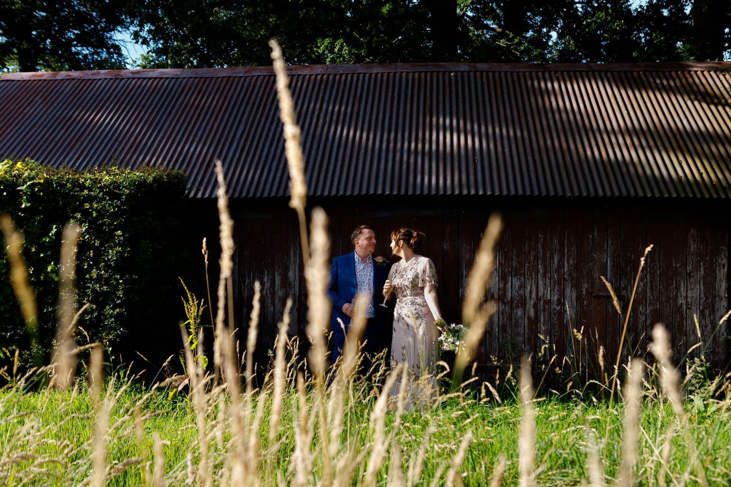Rural barn setting with couple visible through tall summer grasses.