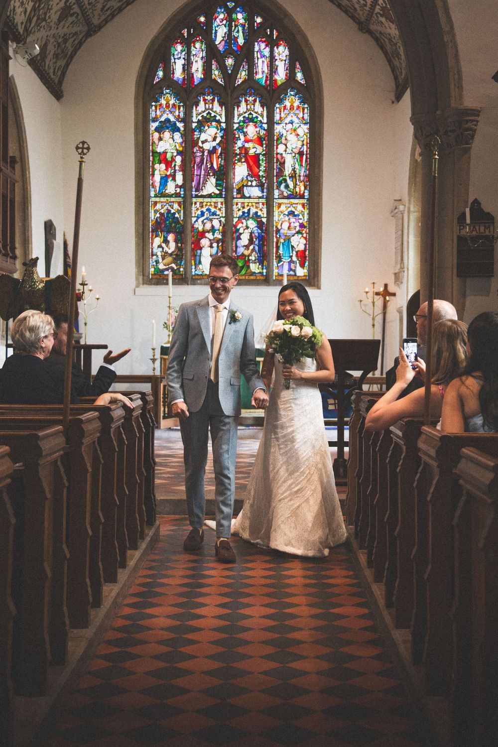 A wedding couple walks down the aisle of a church with beautiful stained glass windows.