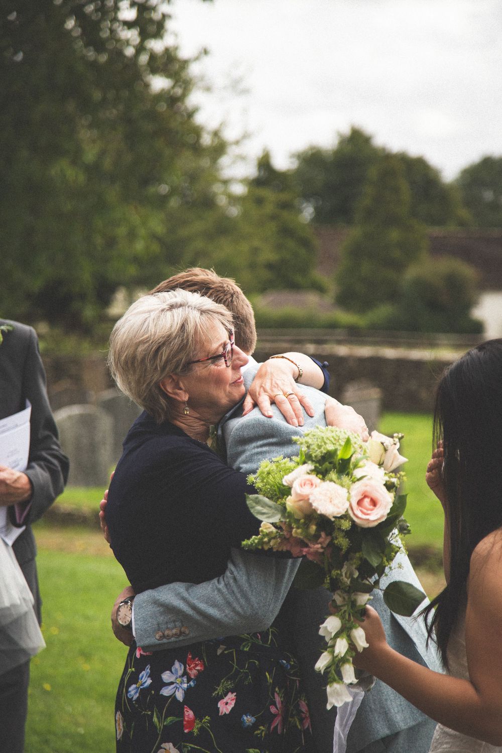 Emotional wedding day hugs exchanged in a garden setting.