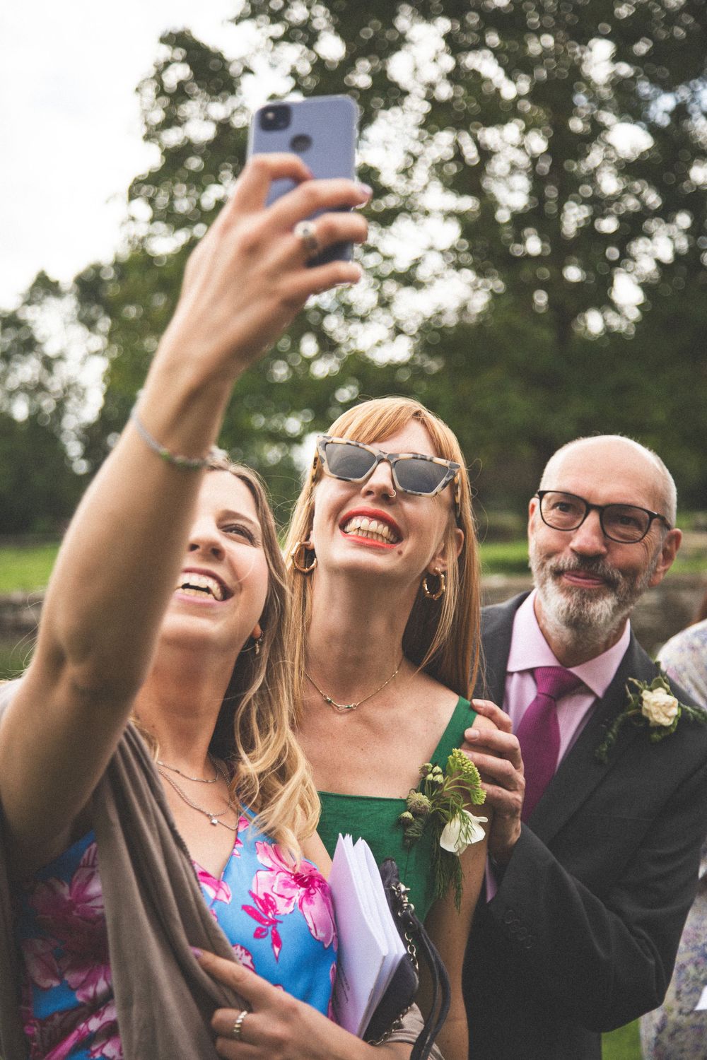 Wedding guests taking cheerful selfies during outdoor celebration.