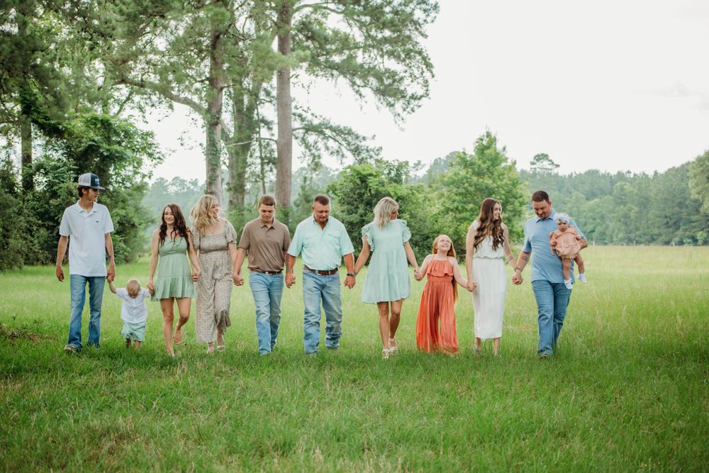 Large family group walking together through sunny green field in casual summer outfits.