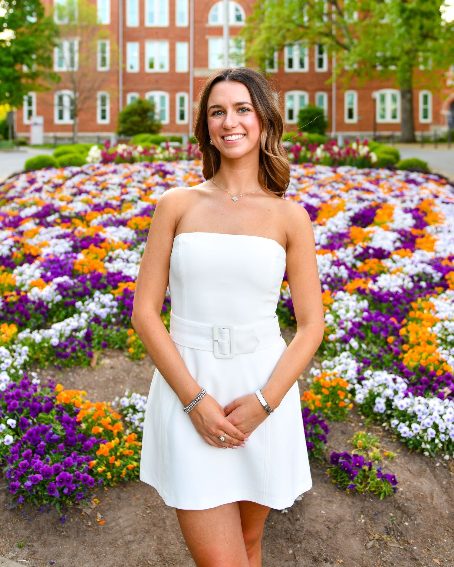 Portrait in front of colorful flower garden and brick building.