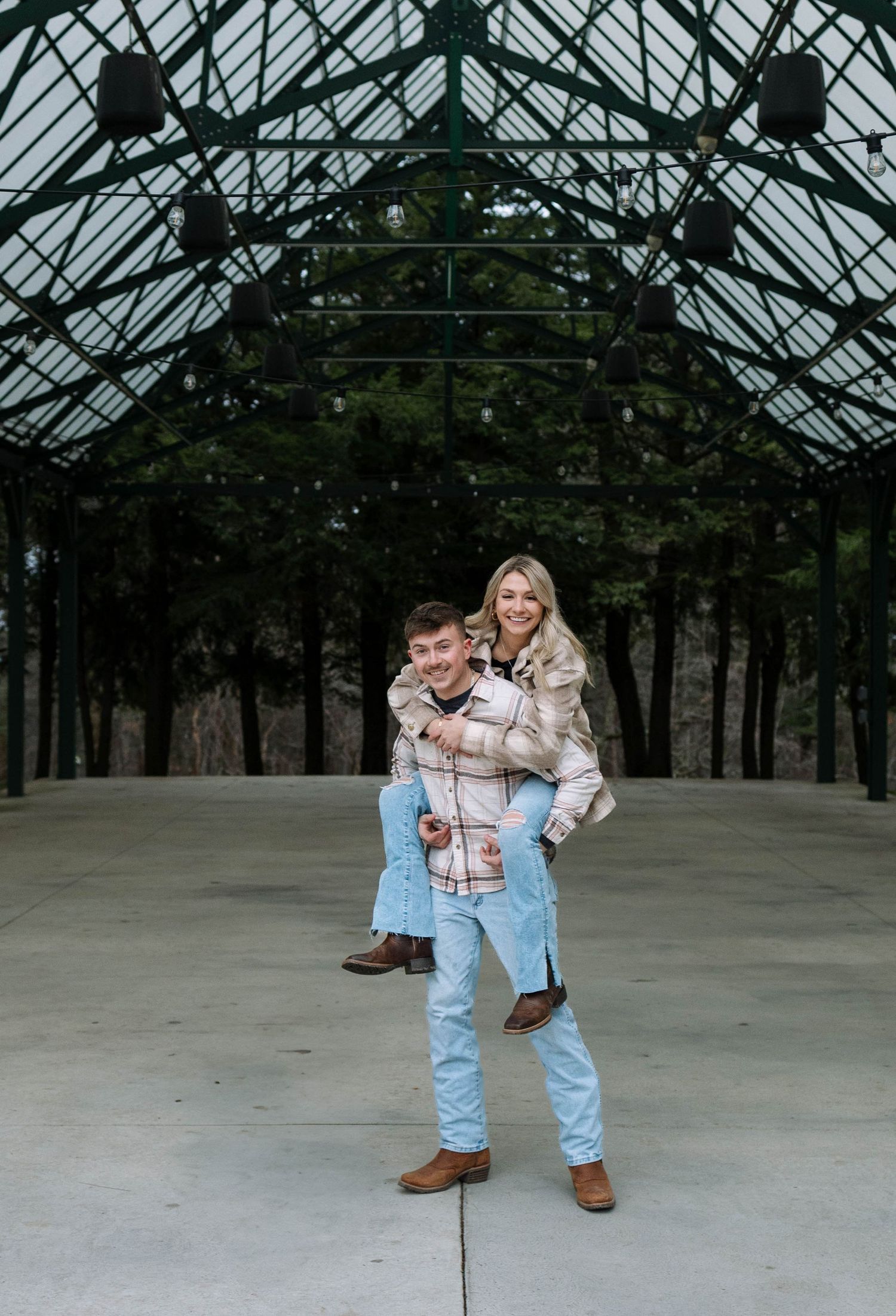 A family poses together under a greenhouse glass ceiling structure with trees visible through the transparent roof.