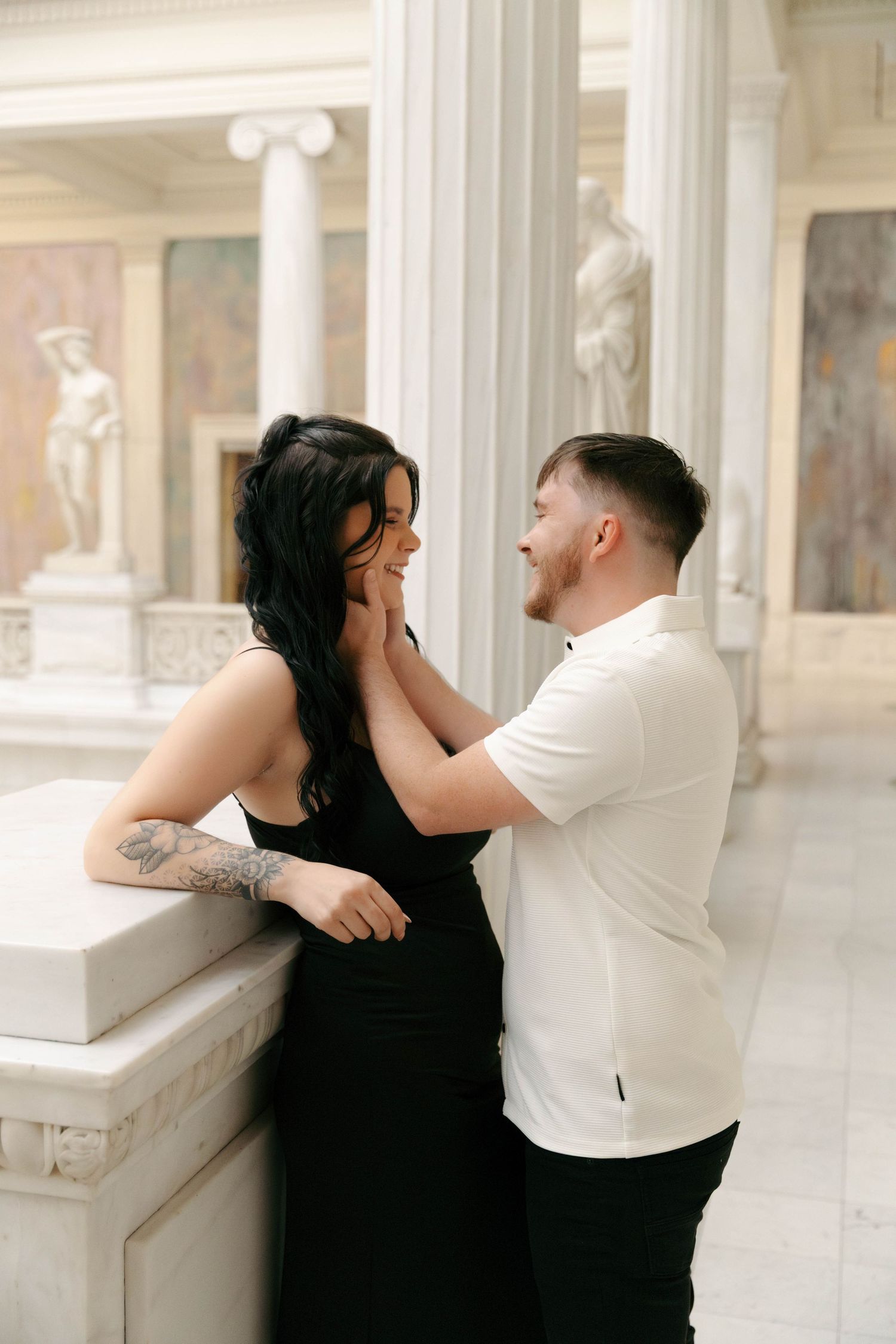 A couple shares a romantic moment in a bright classical architectural space with columns and ornate details.