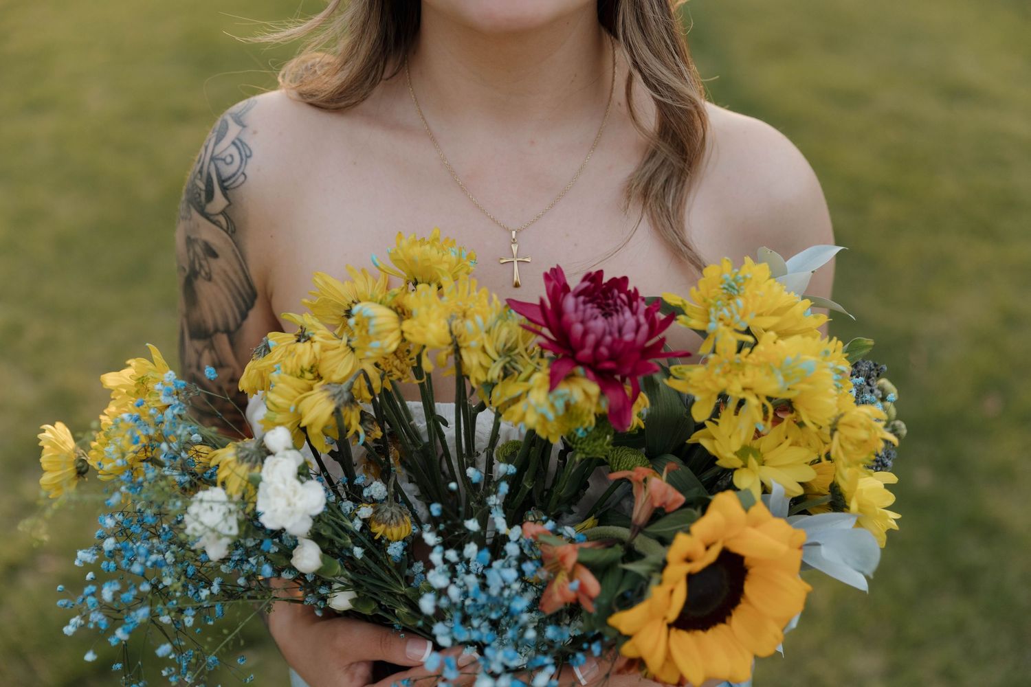 A vibrant bridal bouquet with sunflowers, yellow daffodils, magenta blooms and blue baby's breath against a grassy backdrop.