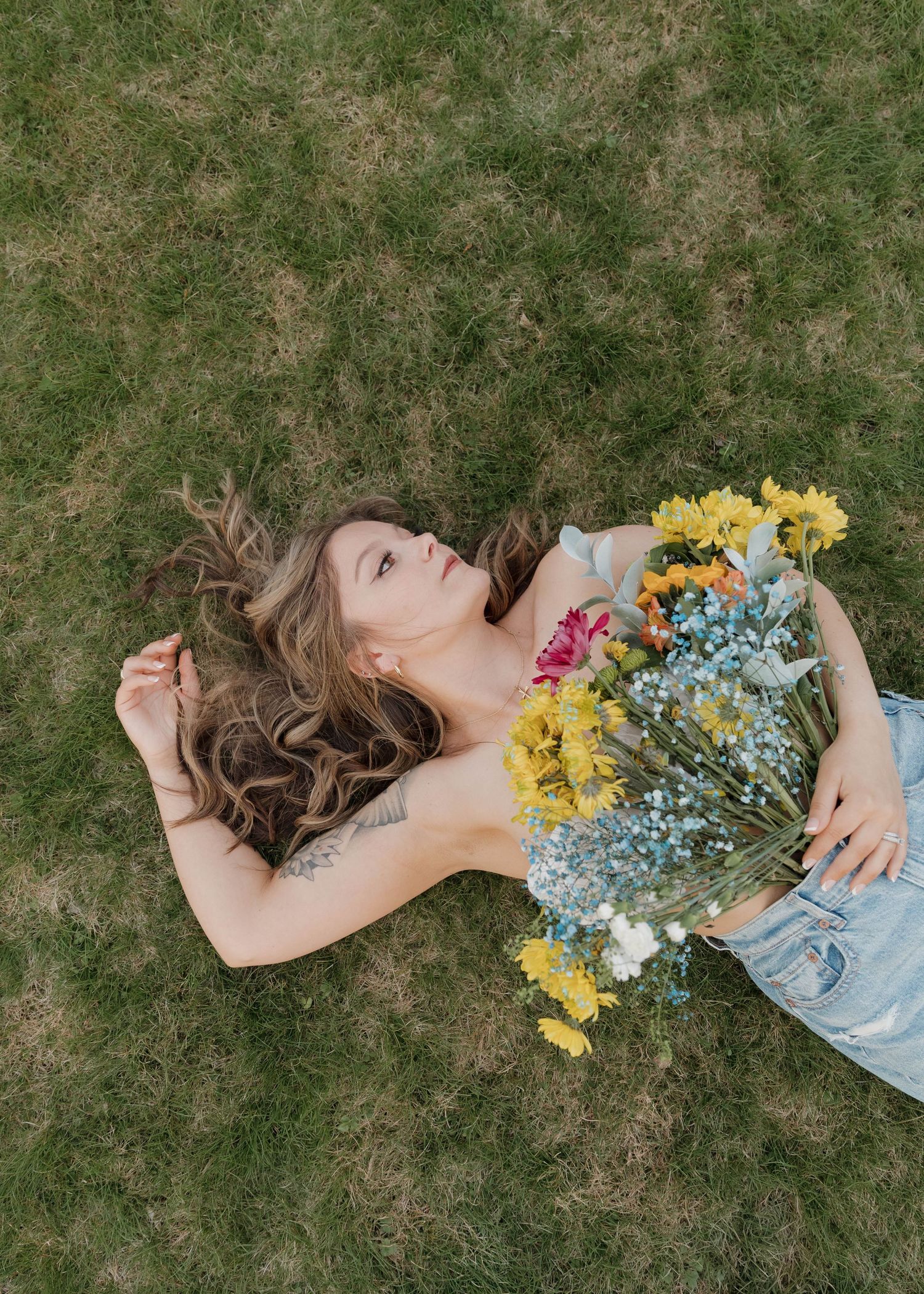 A colorful bouquet of wildflowers rests on someone lying in green grass on a sunny day.