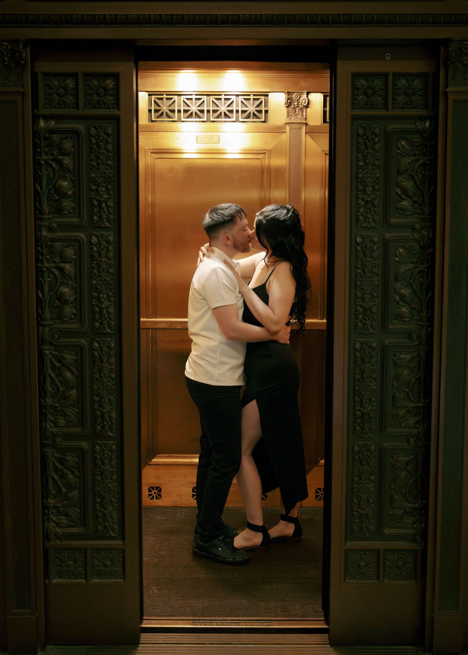 A romantic moment captured in a vintage elevator with ornate art deco doors and warm lighting.