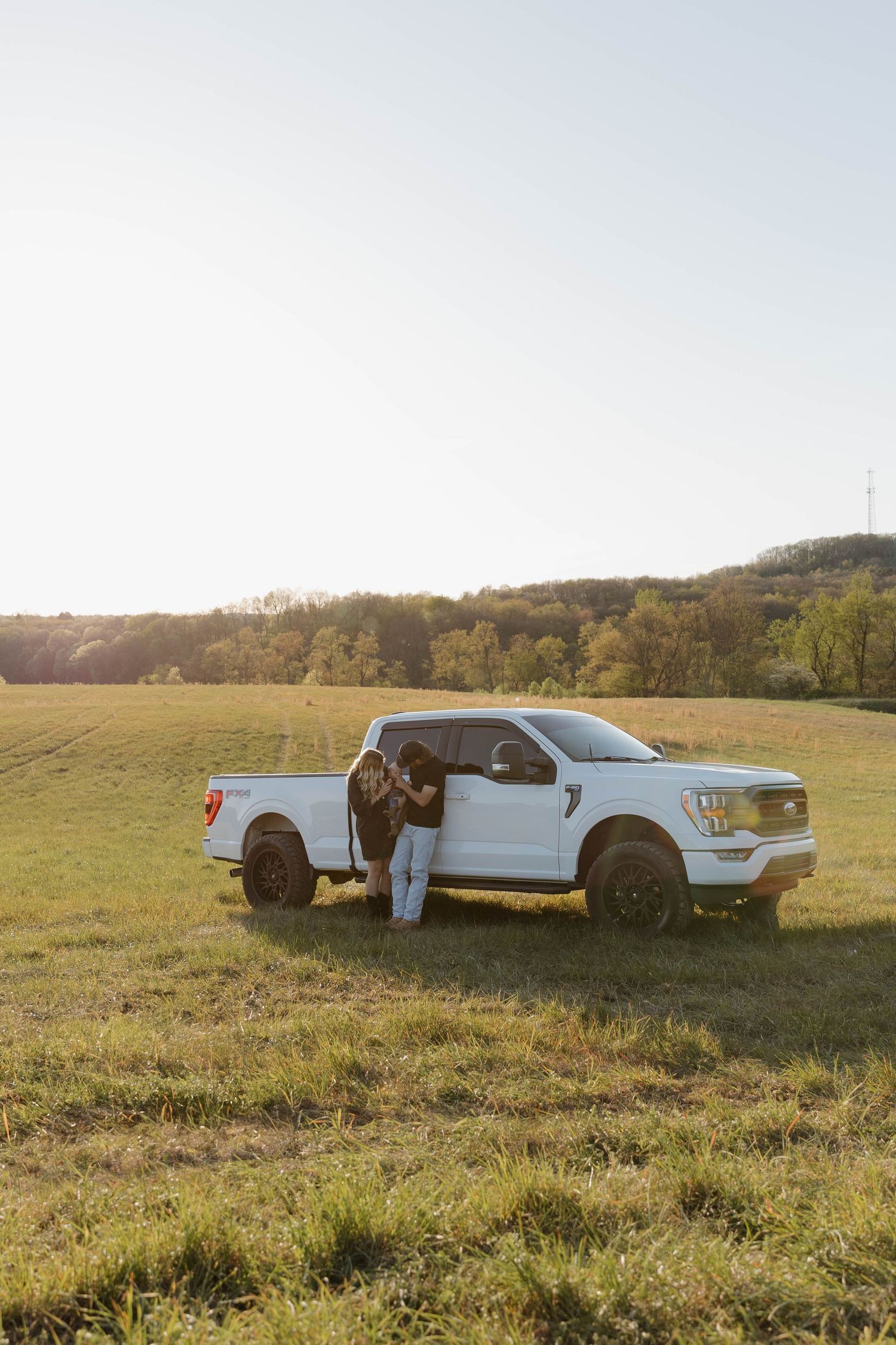 White Ford pickup truck parked in a grassy field during golden hour sunset with rolling hills in the background.