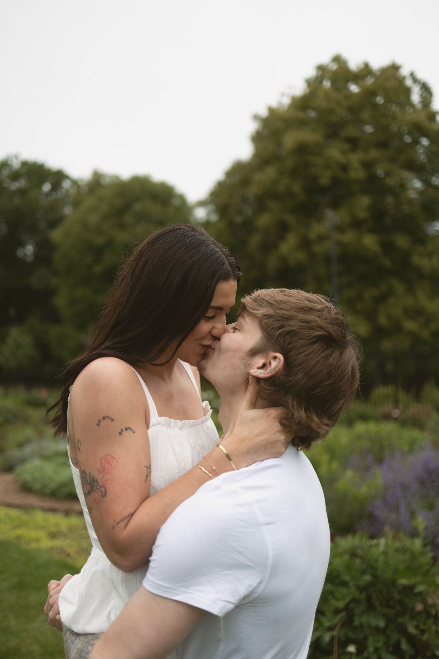 A romantic couple embraces in a garden with lavender flowers and green trees in the background.