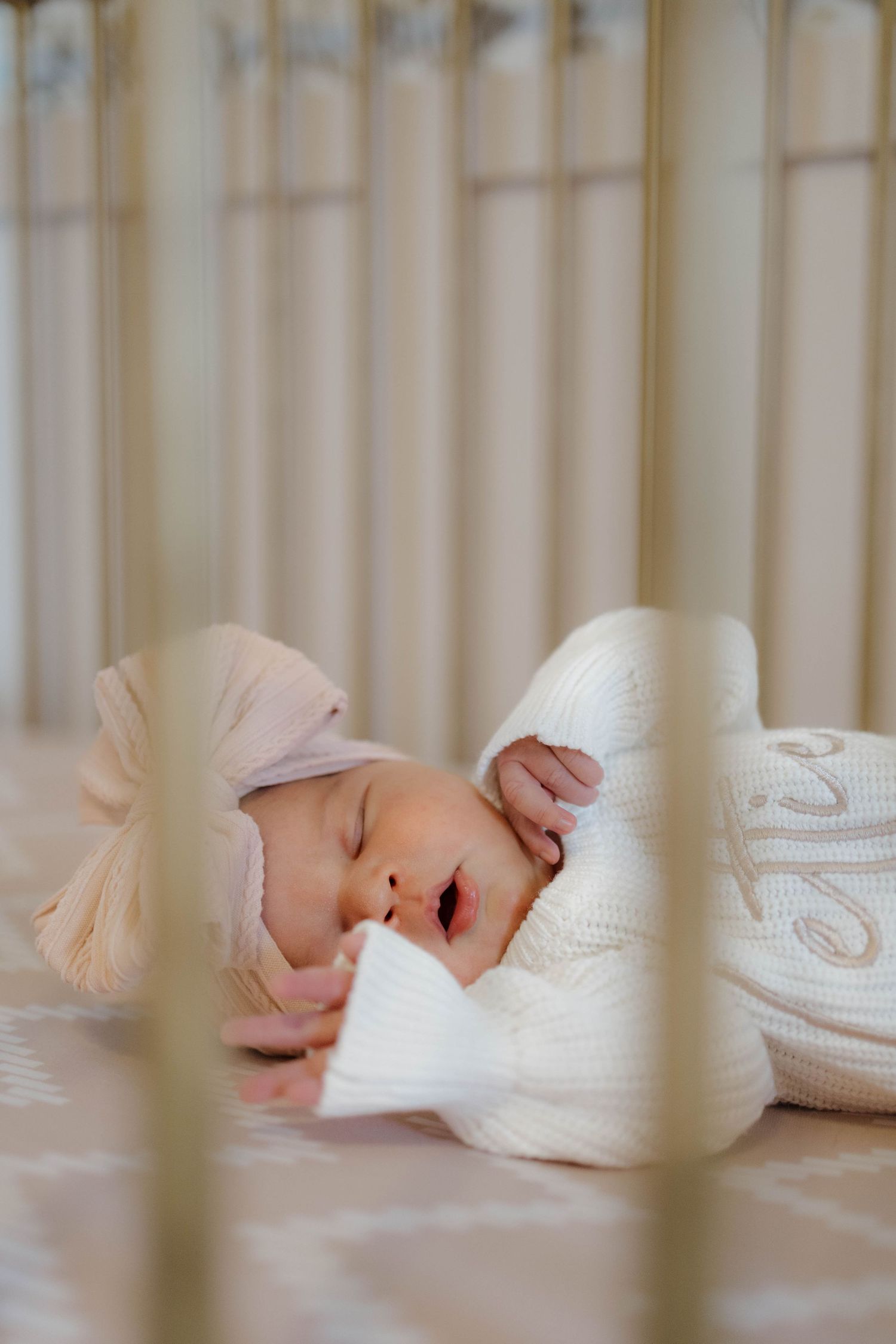 A sleeping baby dressed in white rests peacefully in a crib viewed through the slats.