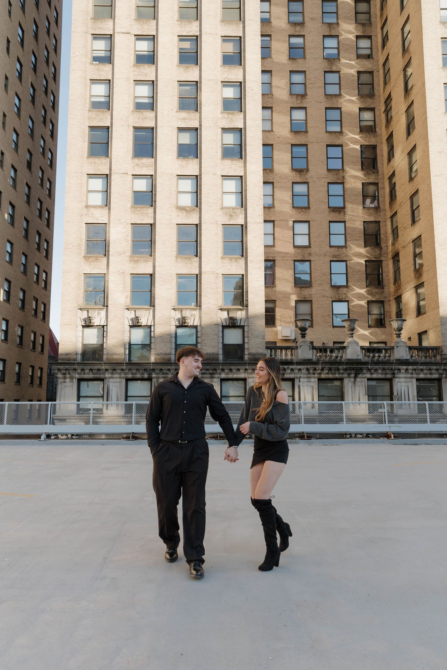 A couple ice skating together at an outdoor rink surrounded by tall city buildings on a winter day.
