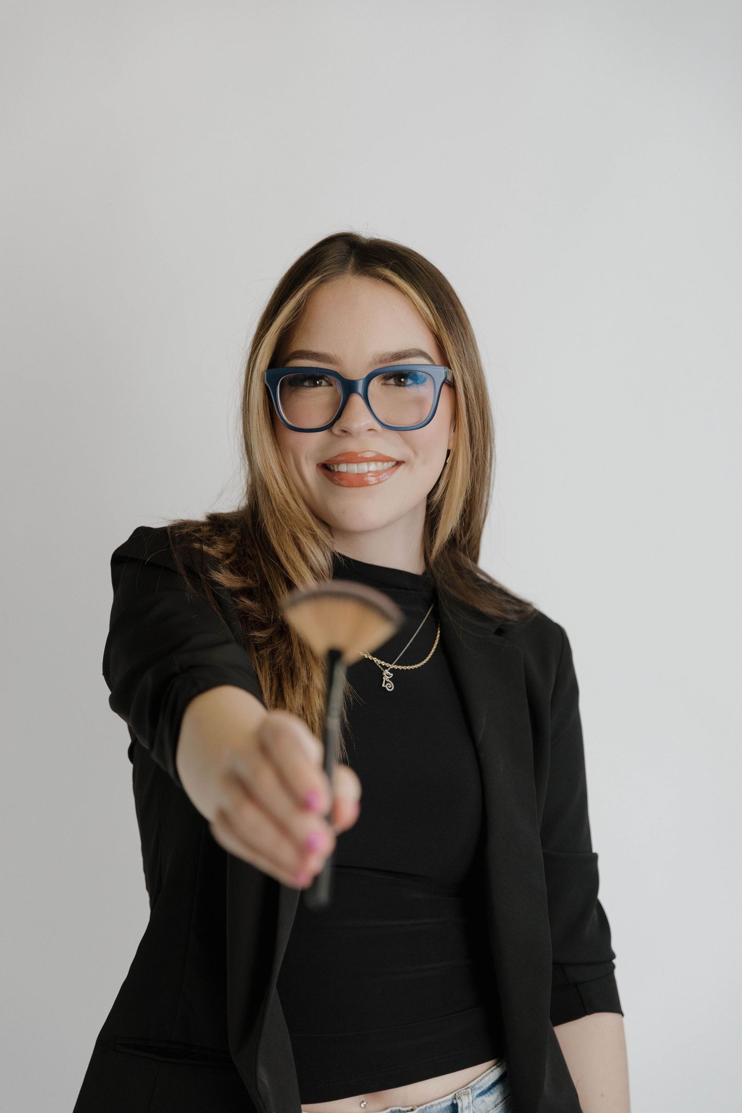 Professional wearing blue glasses and a black blazer holds out an object against a white background.