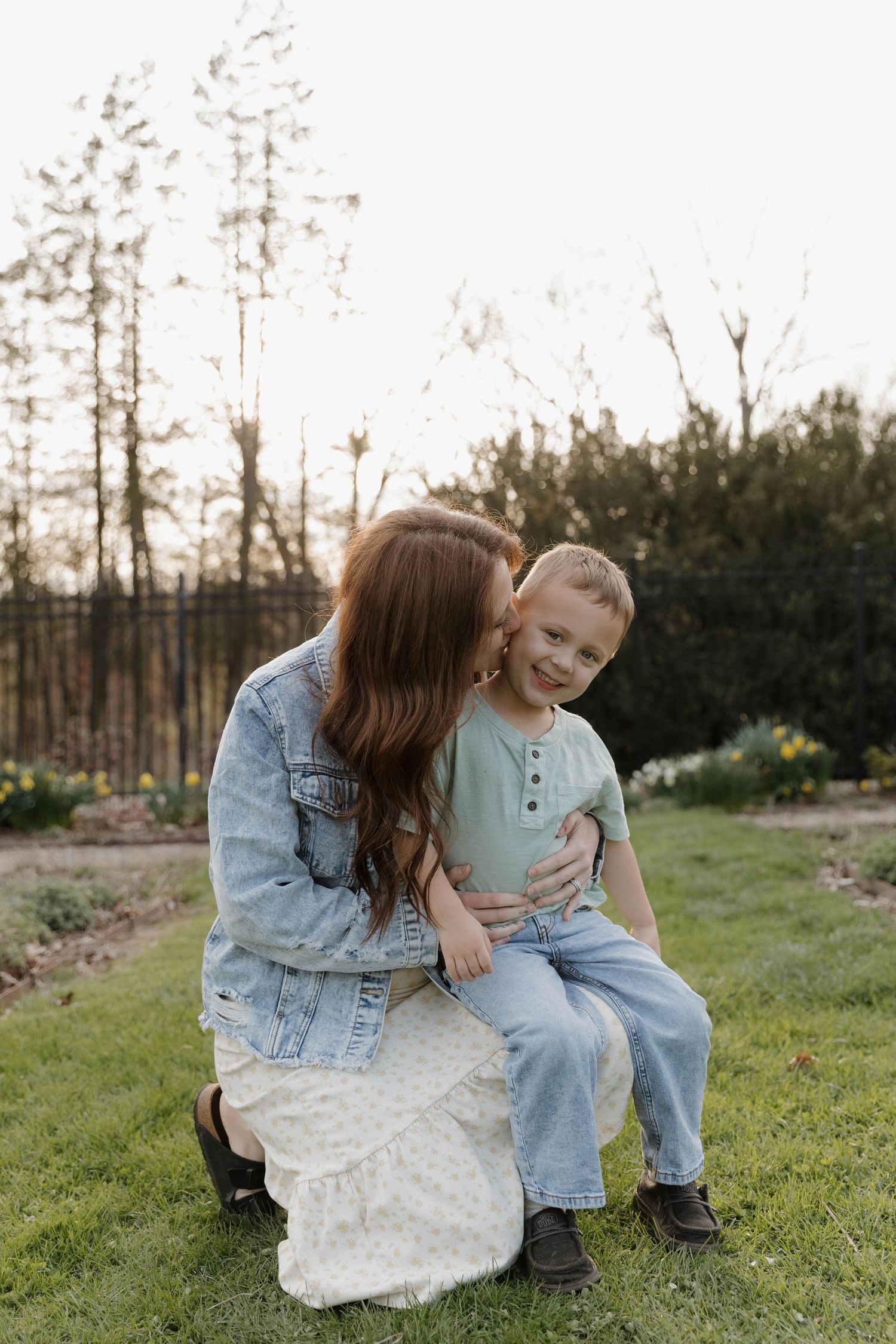 Sweet candid moment between parent and child sharing laughter together on grass at sunset in outdoor garden setting.