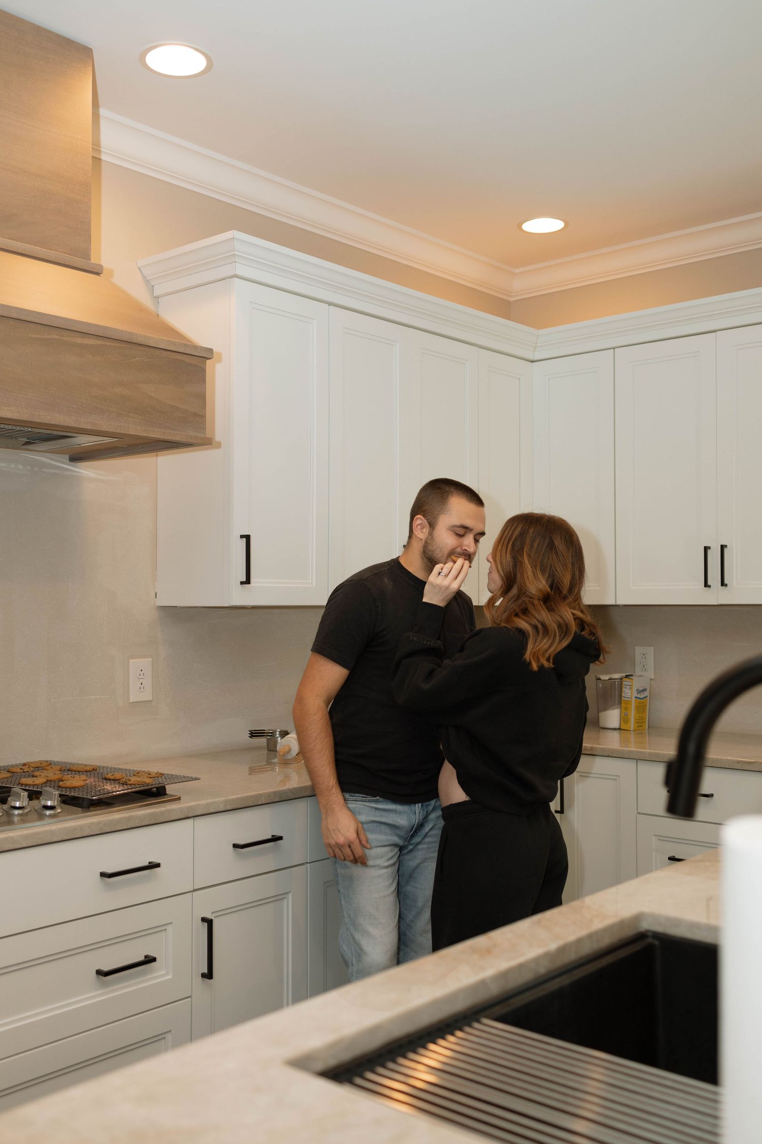 A couple shares a romantic moment in their modern white kitchen with recessed lighting and quartz countertops.