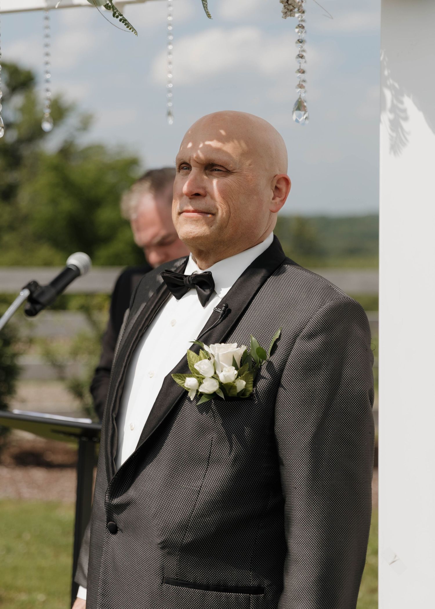 A groom in a black tuxedo and bow tie stands at the altar with a white boutonniere.
