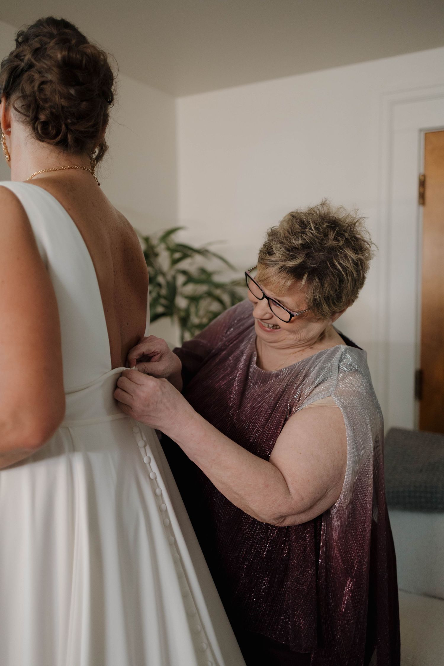 Someone helps adjust the back of an elegant white wedding dress during pre-ceremony preparations.