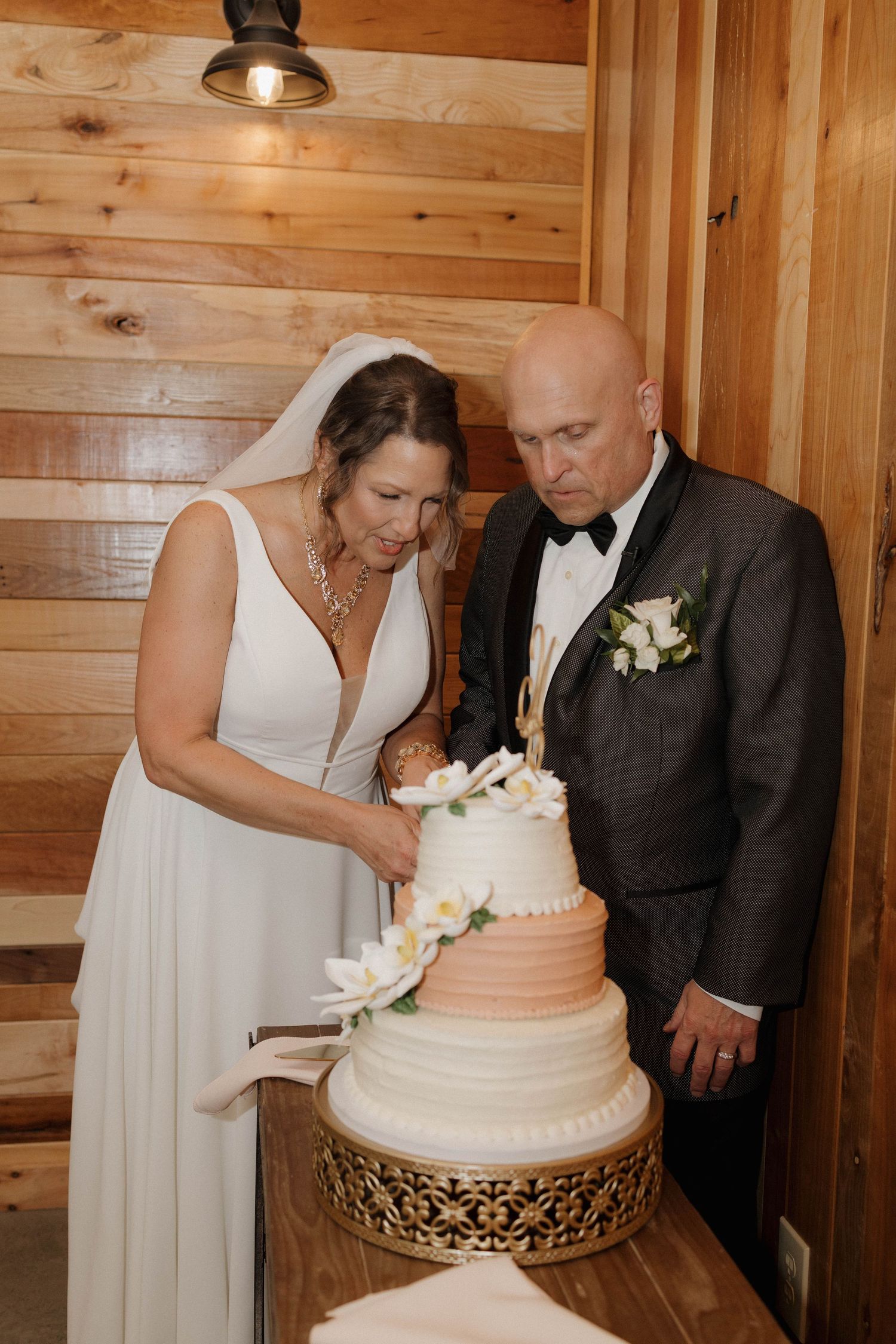 A couple cutting into their elegant three-tiered wedding cake in a rustic wooden venue.