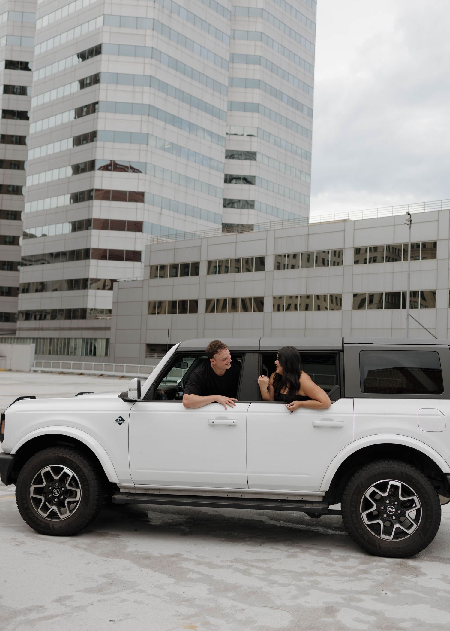 A white Ford Bronco parked in front of a modern office building with glass windows and concrete exterior.