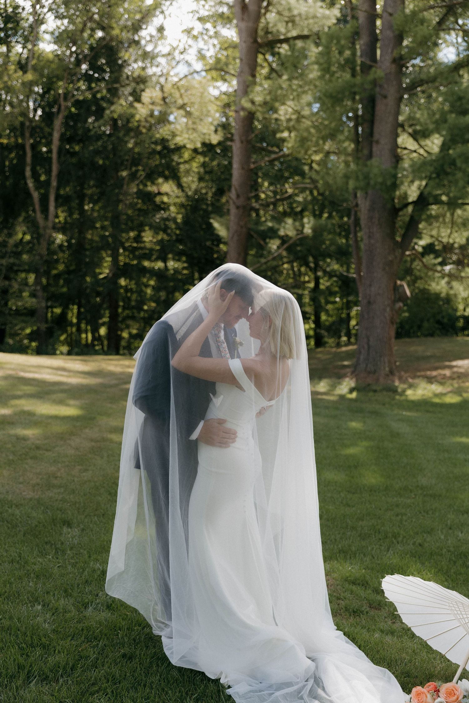 Elegant wedding photos showing ethereal white veil flowing in a natural outdoor setting with trees.
