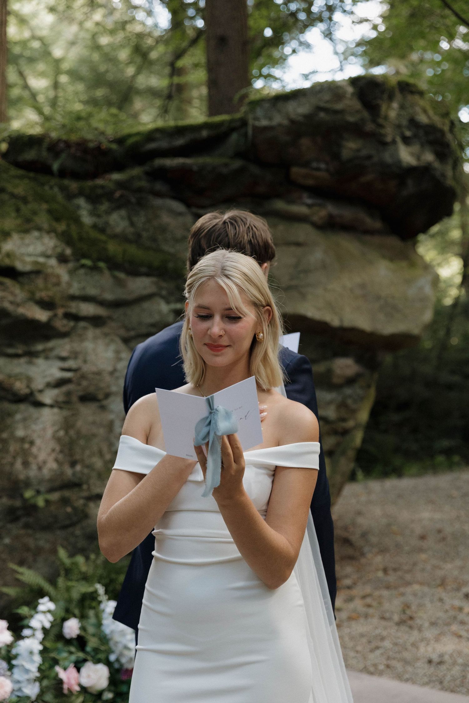 Person in white wedding dress wipes tears from their eyes during an emotional outdoor photoshoot.