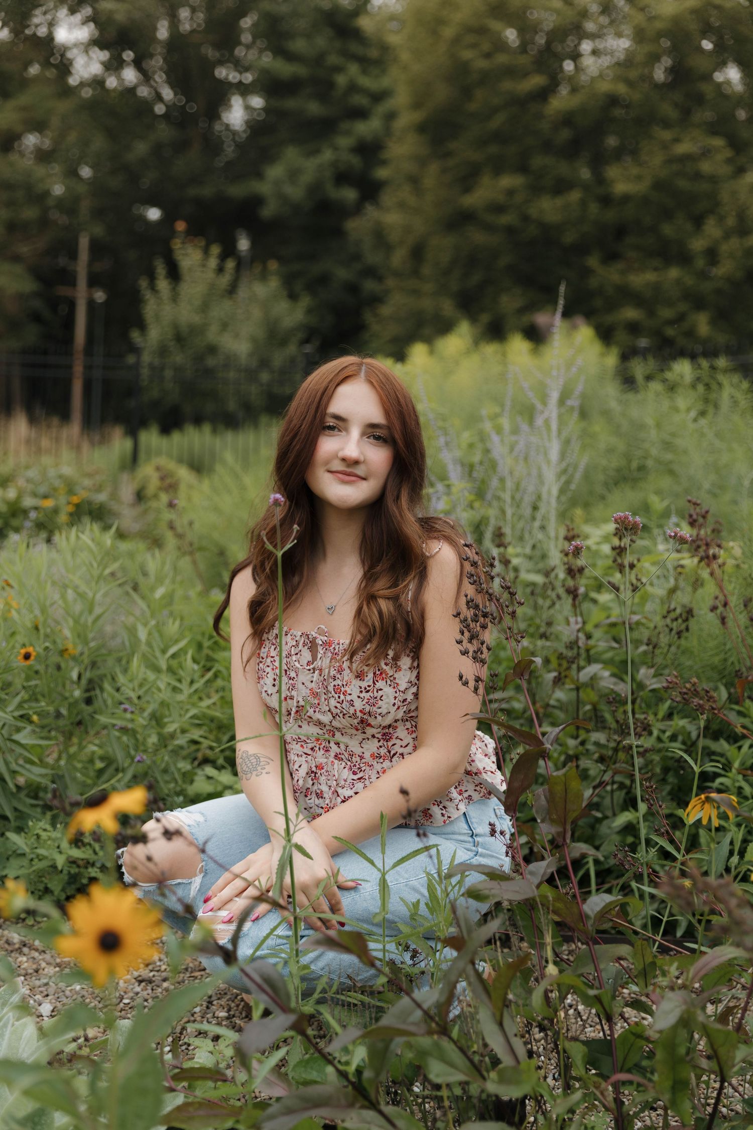 A person sits among wildflowers and greenery wearing a floral sundress in a garden setting during summer.