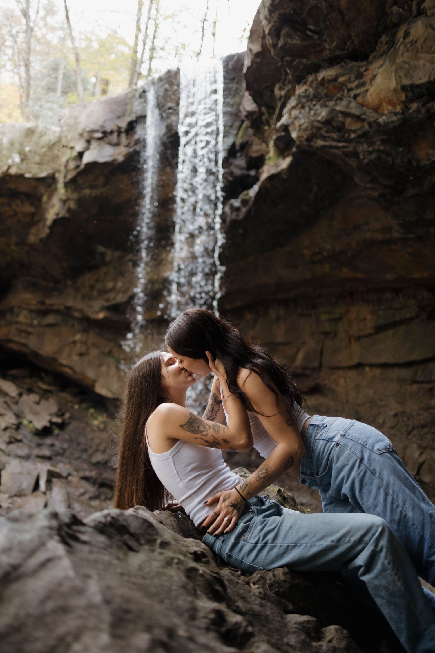 A romantic moment captured at a scenic waterfall cave with rock formations in the background.