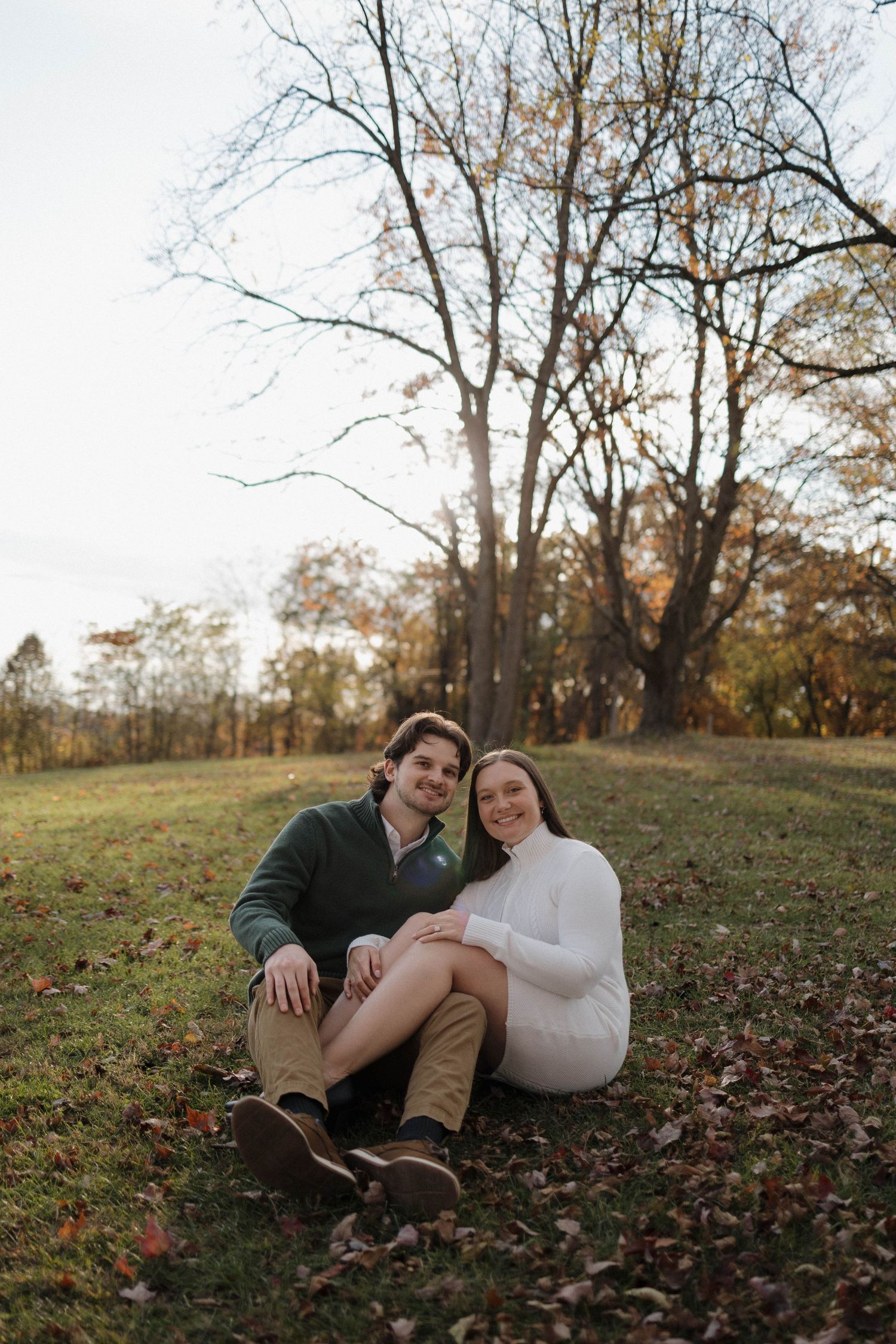 A couple lounges together on autumn leaves during a romantic outdoor photoshoot at sunset.
