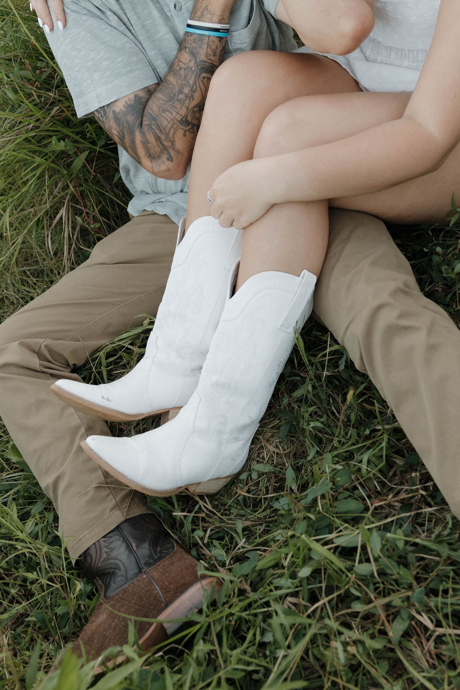 Couple lounging on grass wearing contrasting boots - white cowboy boots and brown work boots.