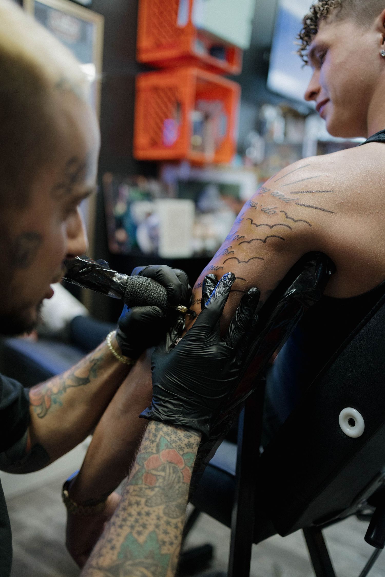 A tattoo artist wearing black gloves works on creating a new design on a customer's arm in a studio setting.