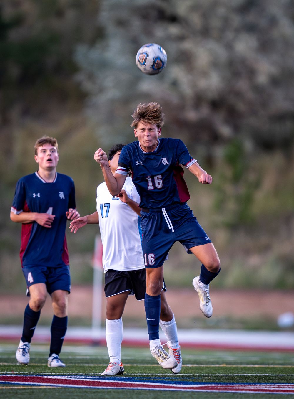 Soccer player leaps high to head the ball during an intense match on a turf field.