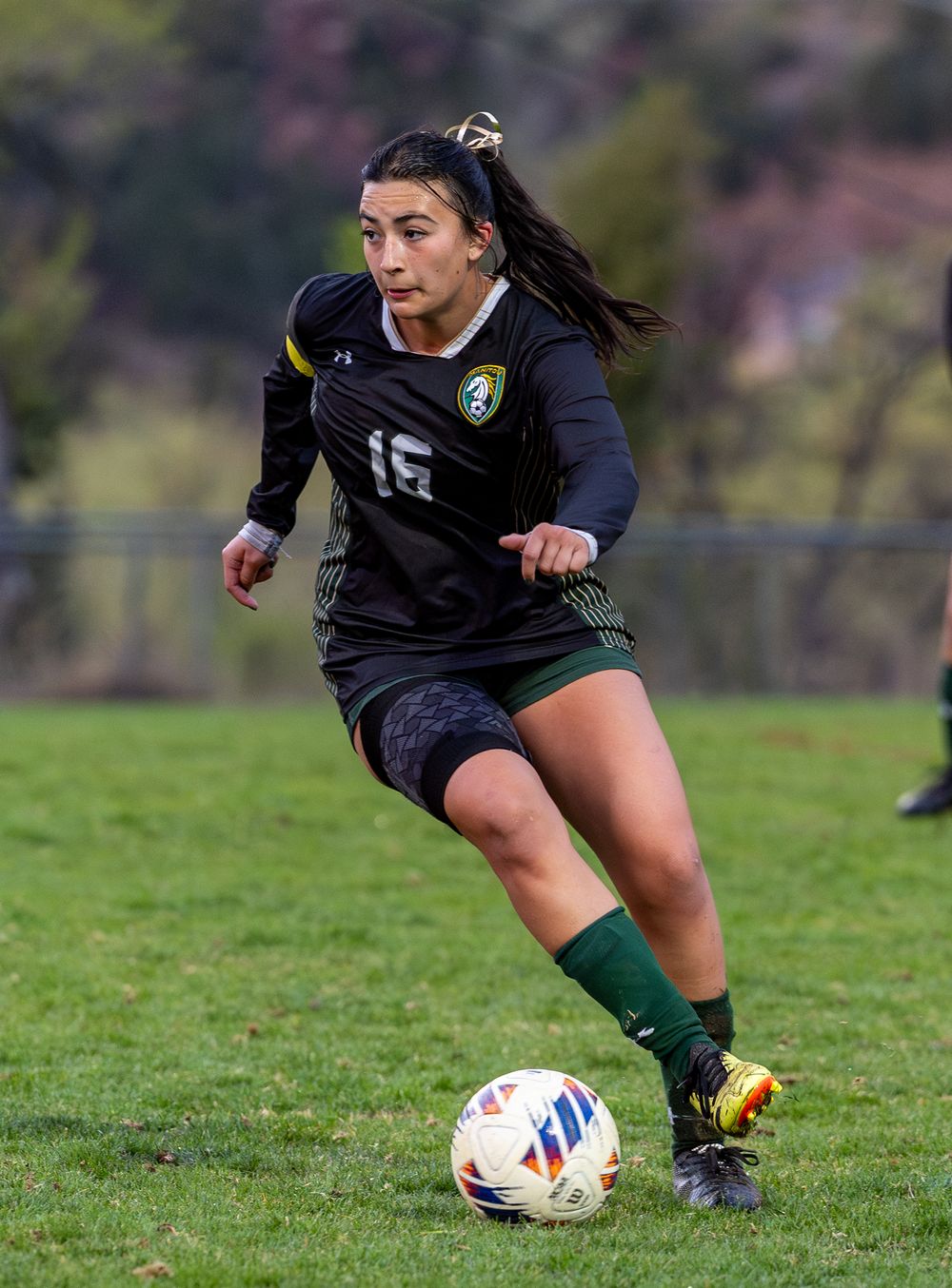 Soccer player in dark uniform dribbles ball during match on grass field.