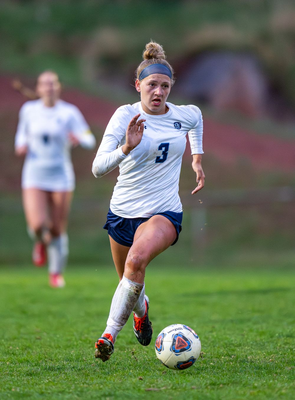 Soccer player in white uniform sprints with ball during competitive match.