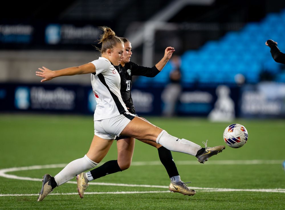 Two soccer players compete for possession of the ball during an intense match on a turf field at night.