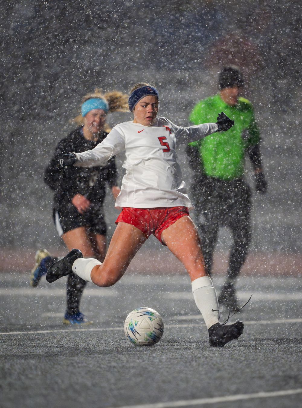 Soccer players battle for ball control during intense match in heavy snowfall.