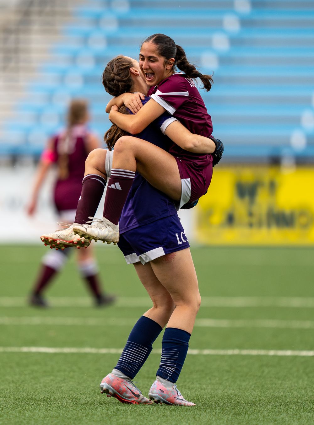 Soccer players celebrate with an emotional embrace and jumping celebration on the field during a match.