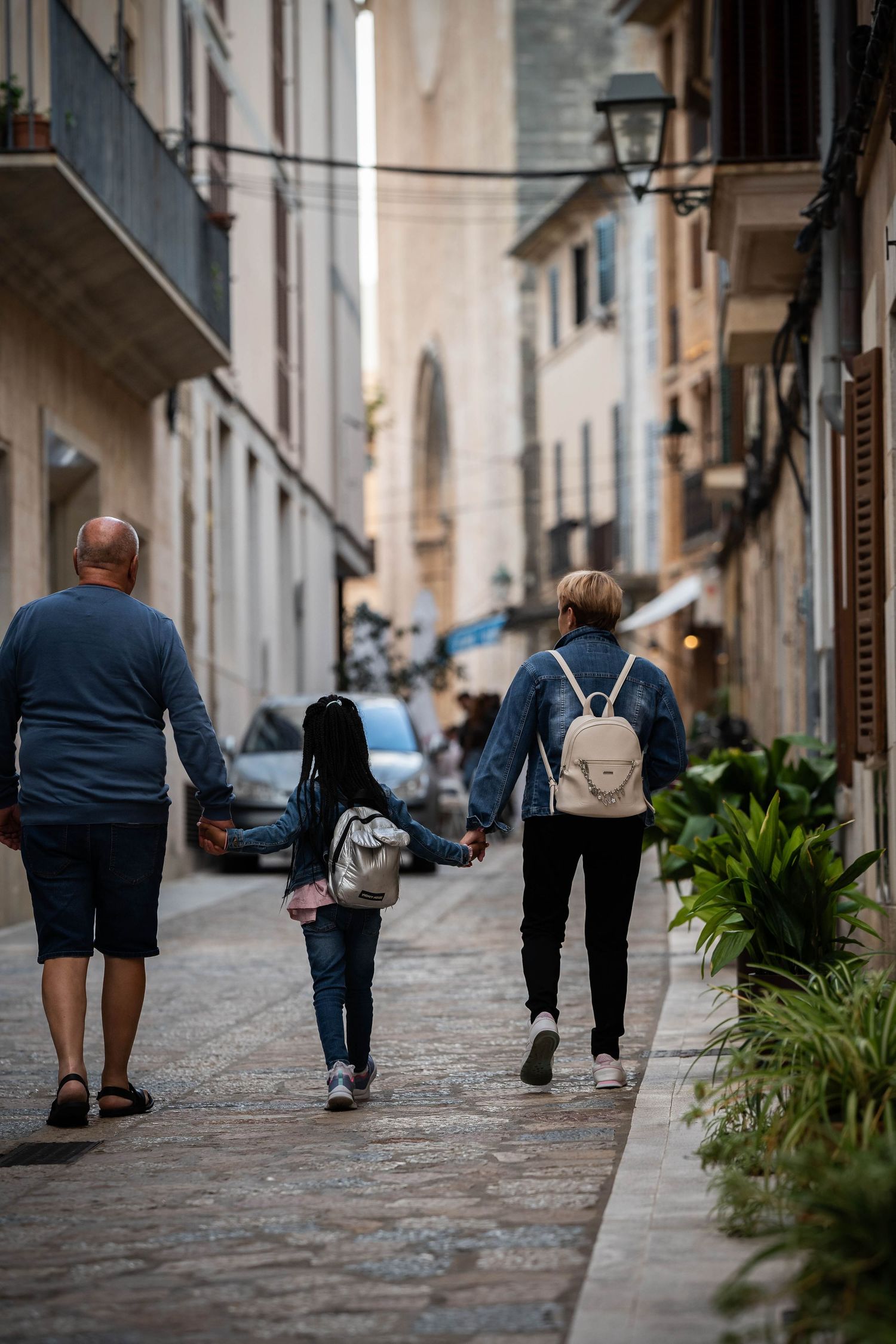 Family walking together down narrow cobblestone street in European city.
