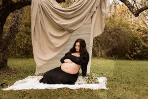 Outdoor maternity photoshoot in natural setting with beige backdrop and white blanket on grass.