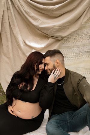 A couple in casual attire share an intimate moment against a draped beige fabric backdrop.