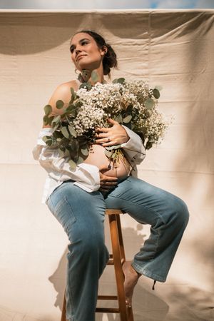 A dreamy portrait featuring a white floral bouquet with eucalyptus, white top and blue jeans against a beige backdrop.