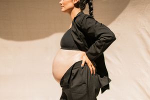 Artistic maternity photo showing a side profile in dramatic black clothing against a neutral beige backdrop.