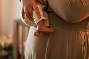 A parent's hands gently cradle tiny newborn feet in soft warm lighting.