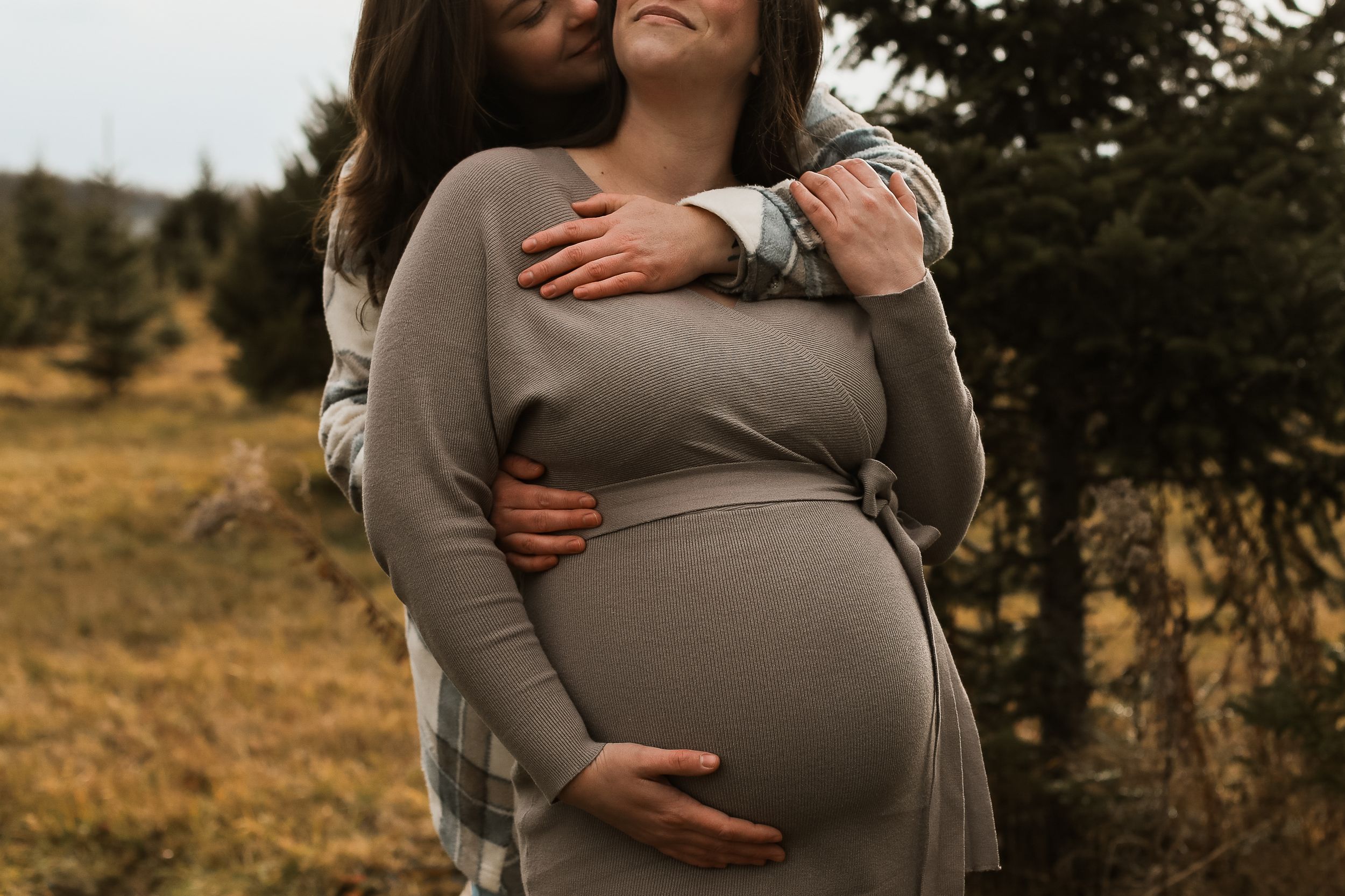 A couple embraces tenderly during a maternity photoshoot in a golden field at sunset.