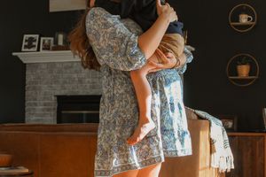 Two people hug in flowy blue floral dresses in front of a stone fireplace at home.